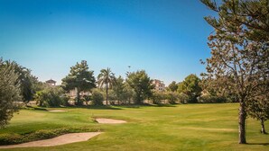 Un parcours de golf avec des bunkers de sable, des arbres et un ciel bleu dégagé.