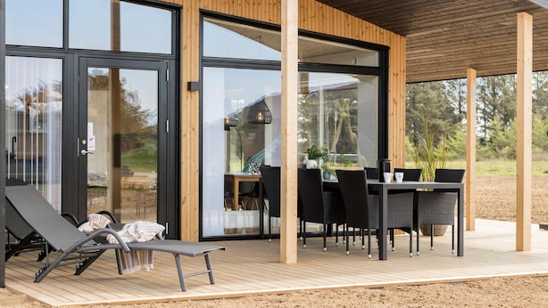 Un espacio exterior techado con terraza de madera, una mesa con sillas y un sillón de descanso.