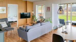 Una sala de estar moderna con un sofá gris, piso de madera, un televisor de pantalla plana y un comedor con mesa y sillas.