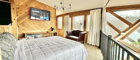 Un dormitorio con una cama grande, techo de madera, televisor montado en la pared, candelabro y vistas a través de una ventana.