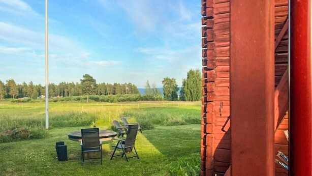 Blick auf eine grüne Außenanlage mit Holzbauten, einer Fahnenstange und einem Tisch mit Stühlen.