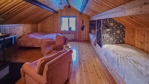 Ein gemütliches Schlafzimmer im Dachgeschoss mit Holzwänden und geneigter Decke. Es beinhaltet ein Bett, eine kleine Couch und ein Fenster, das für natürliches Licht sorgt.