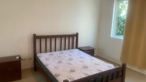 Een slaapkamer met een houten bed, een nachtkastje en een raam met gordijnen.