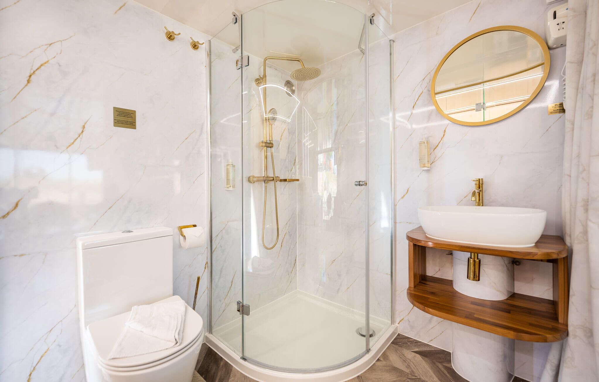 Une salle de bain moderne avec une douche à parois de verre, un lavabo blanc avec un robinet doré et un meuble-lavabo en bois.