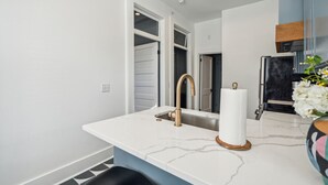 Een moderne keuken met een witte marmeren aanrecht, een gouden kraan en een zwarte koelkast.
