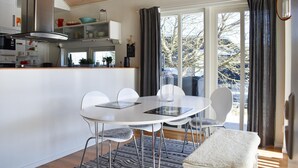 Une cuisine moderne avec des armoires blanches, une hotte en acier inoxydable et un coin repas comprenant une table et des chaises blanches.