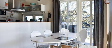 Een moderne keuken met witte kasten, een roestvrijstalen afzuigkap en een eethoek met een witte tafel en stoelen.