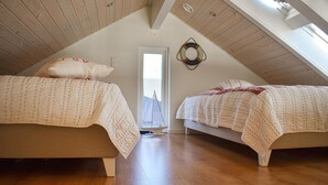 Une chambre avec deux lits, un plancher en bois, un plafond en pente et une petite fenêtre.