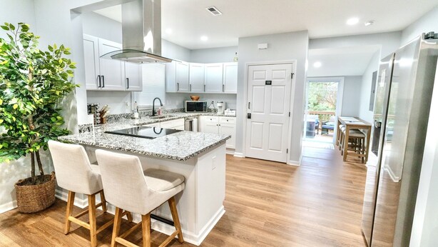 A modern kitchen with white cabinets, a granite countertop, and a central island with bar stools. - Woodruff's Southern Nest, located few blocks from historic downtown Woodruff! (Woodruff)