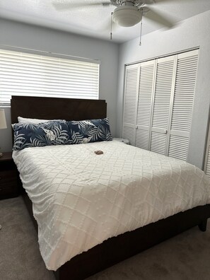 Ein Schlafzimmer mit Bett, Nachttisch, Kleiderschrank und Deckenventilator.