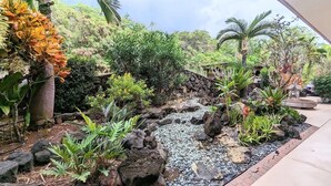 Jardín ajardinado con un pequeño arroyo, diversas plantas y un muro de piedra.