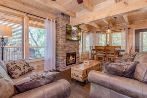 Un intérieur de chalet chaleureux avec une cheminée en pierre, des canapés en cuir et un coin repas.