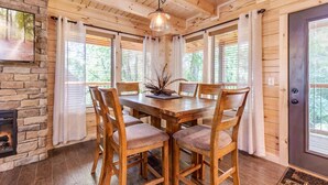 A wooden dining room with a stone fireplace, large windows with blinds, and a chandelier. - Fall & Winter Specials - Dog Friendly! LOCATION, LOCATION, LOCATION!! (Pigeon Forge)