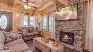 A cozy living room with a stone fireplace, wooden ceiling, and large windows. - Fall & Winter Specials - Dog Friendly! LOCATION, LOCATION, LOCATION!! (Pigeon Forge)