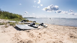Een strand met een surfplank en koptelefoon in het zand, een heldere lucht en een uitzicht op het water in de verte.