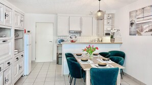 Une cuisine moderne avec des meubles blancs, une table à manger entourée de chaises turquoise et un petit îlot central doté d’un évier.