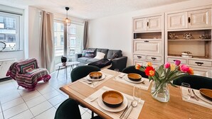 Un salon moderne comprenant un coin repas, un canapé gris, une table à manger en bois dressée avec des assiettes et des bols, et un vase de tulipes.