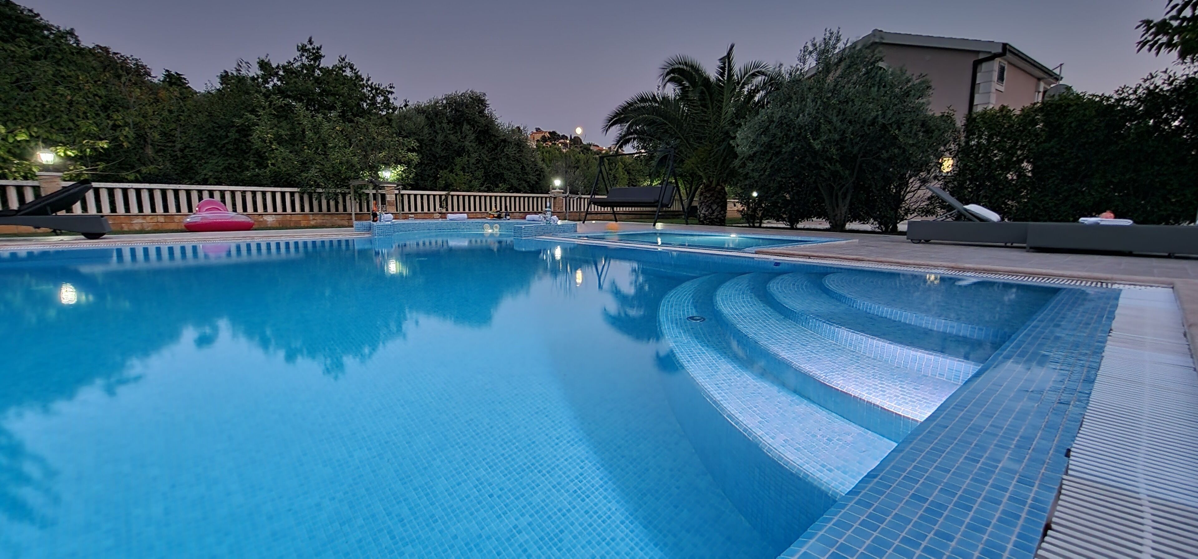 Une piscine dont le bord est revêtu de carrelage, entourée d’une terrasse en bois et de palmiers.