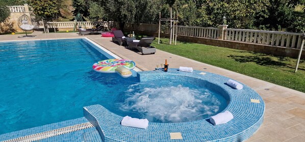 Une piscine avec un jacuzzi, des chaises longues et un matelas gonflable.