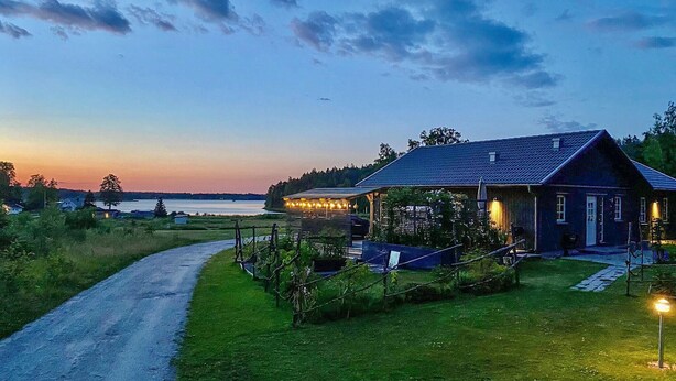 Un chalet rustique doté d’un porche abrité, d’une allée pavée et offrant une vue sur un lac au crépuscule.