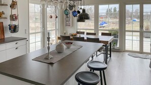 Une cuisine moderne dotée d’un grand îlot central, de tabourets de bar, de luminaires suspendus et de grandes fenêtres offrant une vue sur l’extérieur.