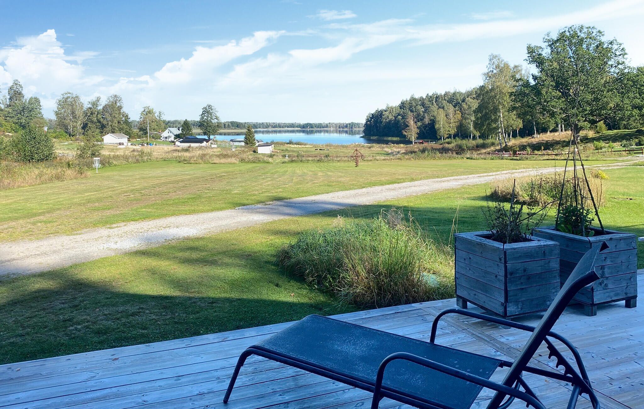 A deck with two lounge chairs overlooking a grassy field and a lake.