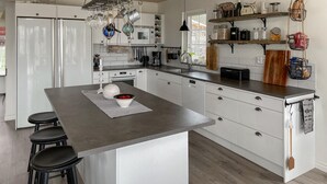 Une cuisine moderne avec des meubles blancs, un îlot central doté de tabourets, des ustensiles de cuisine suspendus et une variété d’accessoires de cuisine.