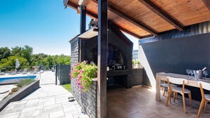 Eine Terrasse mit Steinmauer, Holzbalken, Grill und Pool.