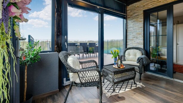 Ein Balkon mit Korbstühlen, einem kleinen Tisch und einem Blumenstrauß.
