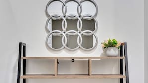 A wall-mounted mirror with a geometric design, a wooden shelf below, and a potted plant on the right.