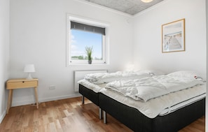Un dormitorio con cama, mesita de noche, ventana con persianas, radiador y un cuadro enmarcado en la pared.