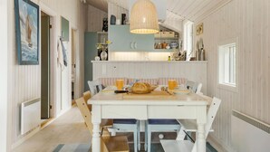 A dining area with a white table and chairs, a wicker pendant light, and a view of the kitchen with a blue cabinet.