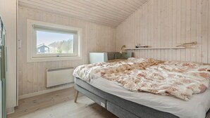 A bedroom with a bed, a window, a radiator, and a shelf with books.