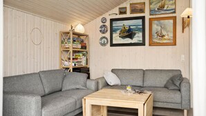 A cozy living room with two grey sofas, a wooden coffee table, and a bookshelf filled with books and puzzles.