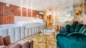 Ett modernt hotellrum med en stor säng, en sittgrupp med ett soffbord i glas och utsikt genom en glasdörr.