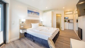 A modern hotel room with a large bed, bedside tables, a desk, and a kitchenette. - Apartments Waterfront (Sagard)
