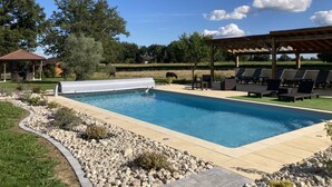 En swimmingpool med ett överbyggt däck, solstolar och en pergola.