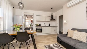 Eine moderne Küche mit weißen Schränken, einem Essbereich mit Glastisch und einem grauen Sofa.