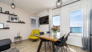 Ein modernes Wohnzimmer mit Esstisch, gelbem Sessel und Meerblick.