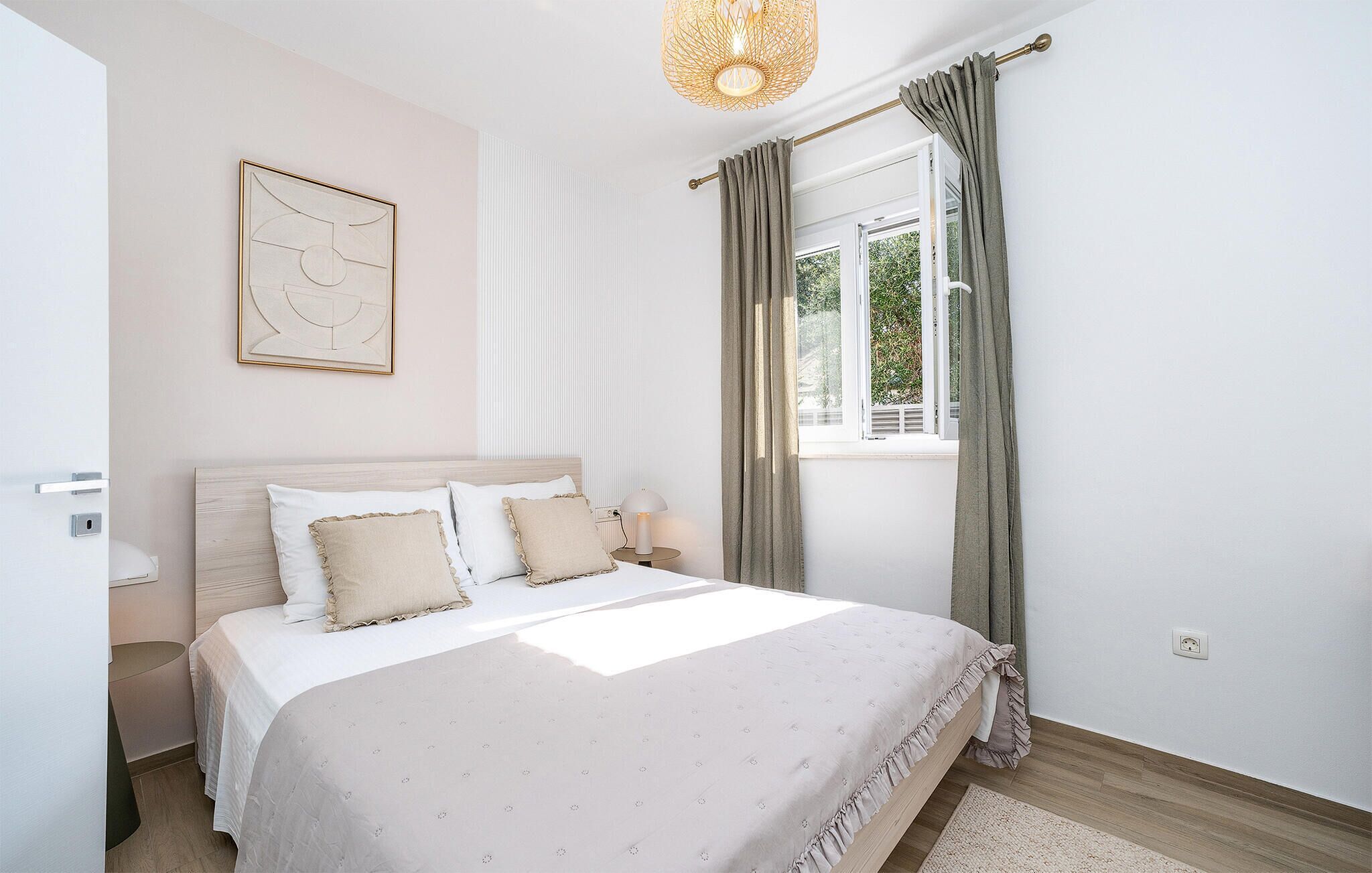 Une chambre à coucher comprenant un lit, une table de chevet, une lampe, une fenêtre avec des rideaux et un luminaire fixé au mur.
