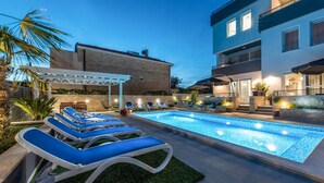 A swimming pool with lounge chairs, a covered seating area, and a stone building in the background. - Nice apartment in Bibinje (Bibinje)