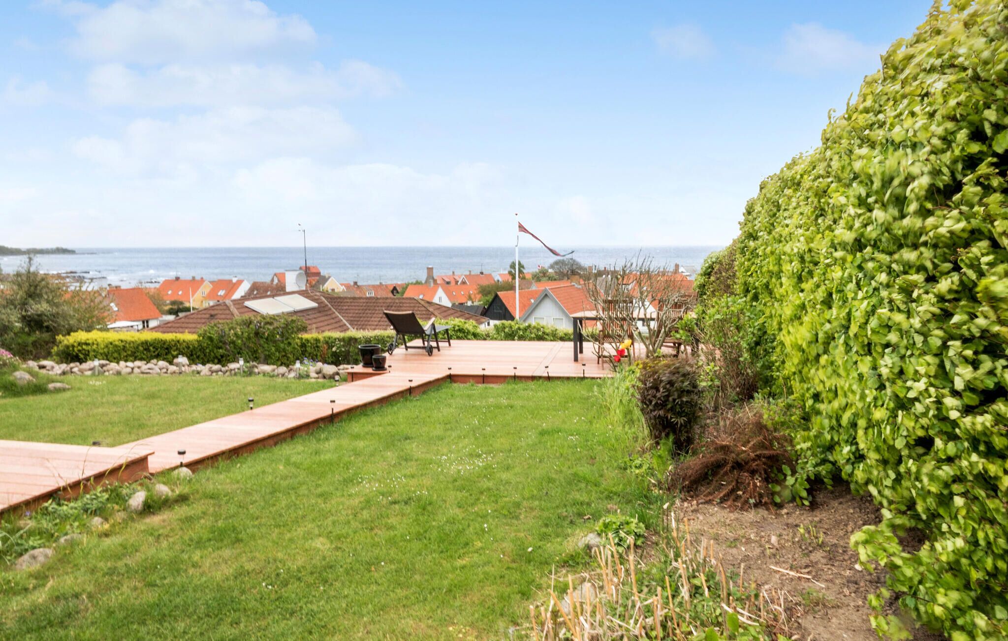 A residential area with a well-maintained lawn, a wooden deck, and a view of the sea.