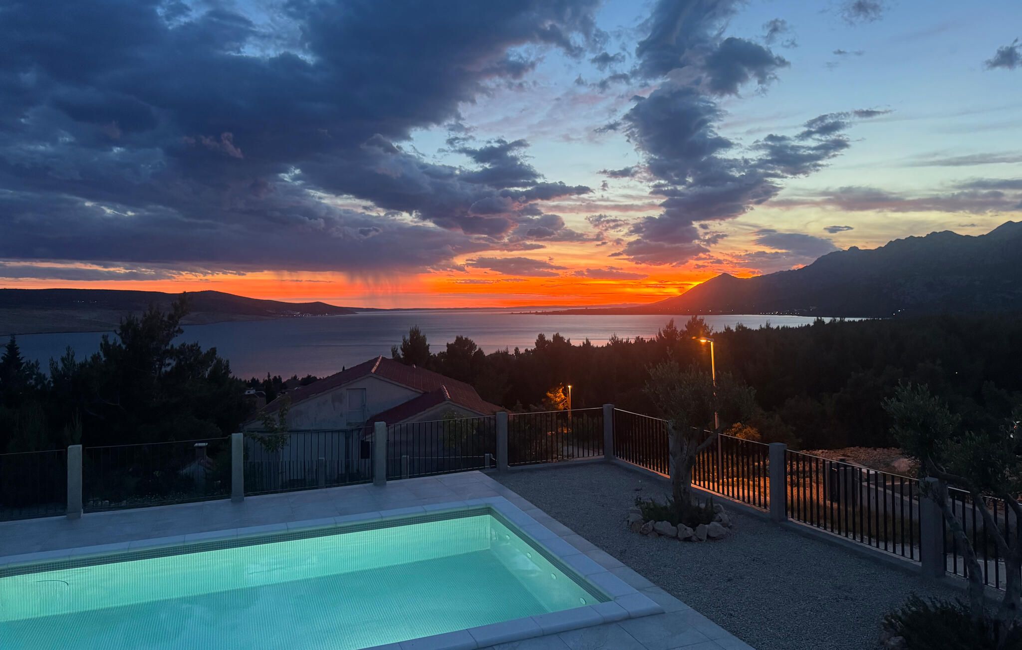 A swimming pool with a view of a sunset over a body of water and mountains.