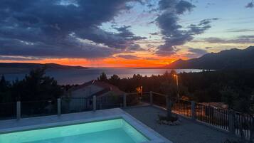 A swimming pool with a view of a sunset over a body of water and mountains.