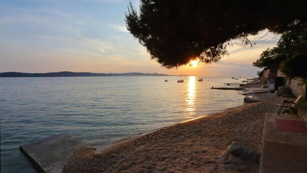 Ein Strand mit Sonnenuntergang, ruhigem Wasser und einer Reihe von Bänken entlang der Küste.