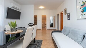 Ein modernes Wohnzimmer mit einer Couch, einem Esstisch mit Stühlen, einem Fernseher und einer Pflanze.