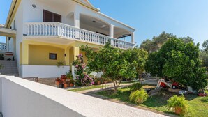 Ein zweistöckiges Haus mit Balkon, umgeben von Grünpflanzen und Blumentöpfen.