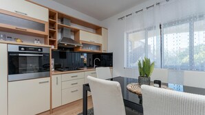 Eine moderne Küche mit Einbauofen, Herd und Dunstabzugshaube. Ein Essbereich mit Tisch und Stühlen sowie ein Fenster mit durchsichtigen Vorhängen.