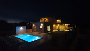 Ein modernes Haus mit Schwimmbad in der Nacht, mit großzügiger Terrasse und einem Balkon im zweiten Stock.