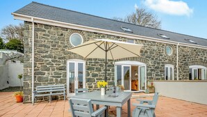 Un bâtiment en pierre doté d’un patio comprenant une table et des chaises, un banc et un grand parasol.